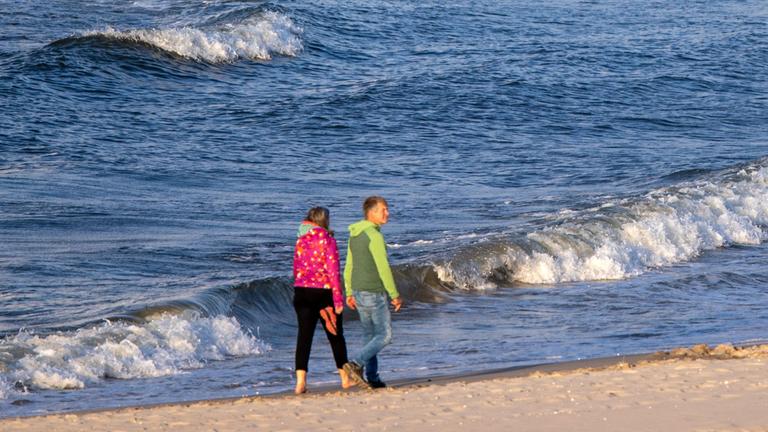 Spaziergänger gehen bei starkem Wind und kräftigem Wellengang auf der Ostsee am Strand der Insel Usedom am 12.06.2021 entlang.
