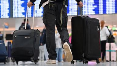 Passagier am Flughafen geht mit zwei Koffern auf Anzeigetafel zu.