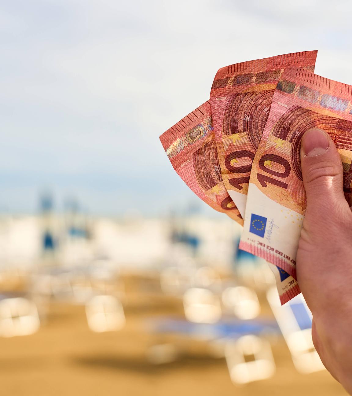 Ein Mann hält Euroscheine vor einer Reihe von Liegestühlen in Italien in der Hand.