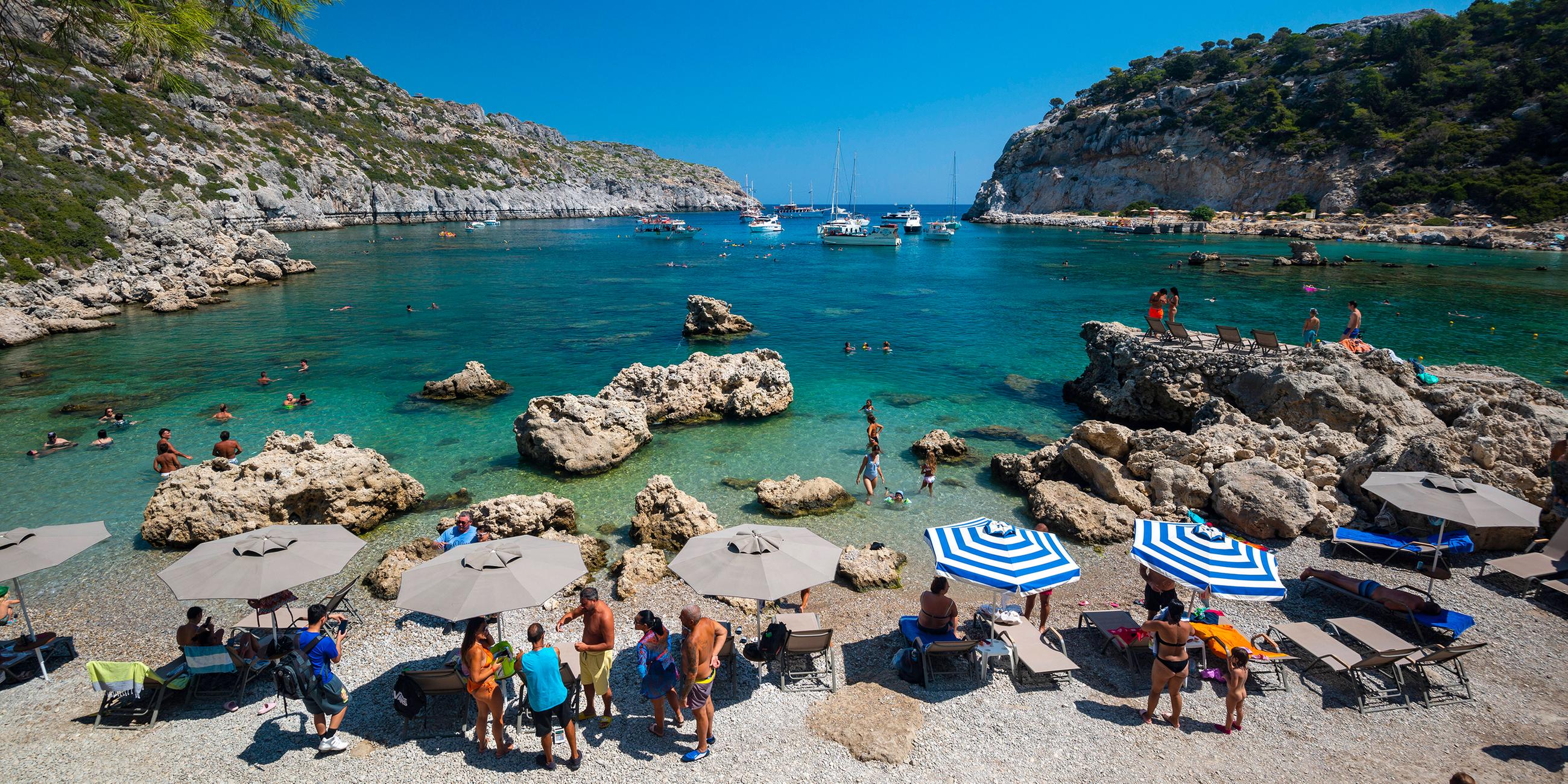 Touristen unter Sonnenschirmen am Strand von Rhodos