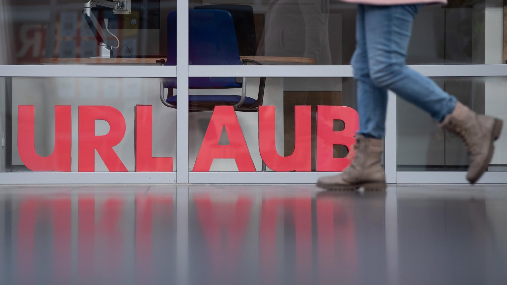 Die Buchstaben Urlaub stehen in einem Schaufenster und ein Mensch läuft daran vorbei.