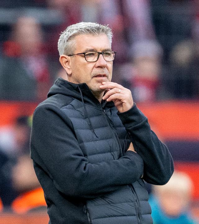 Fußballtrainer Urs Fischer trägt eine schwarze Weste und blickt nachdenklich von der Seitenlinie aufs Spielfeld.