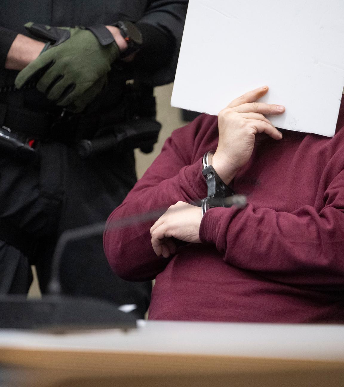 Der Angeklagte sitzt im Saal des Landgerichts Mannheim und verdeckt sein Gesicht. 