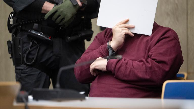 Der Angeklagte sitzt im Saal des Landgerichts Mannheim und verdeckt sein Gesicht. 