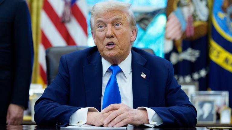 Eine Aufnahme von Trump, wie er an seinem Tisch sitzt und spricht,