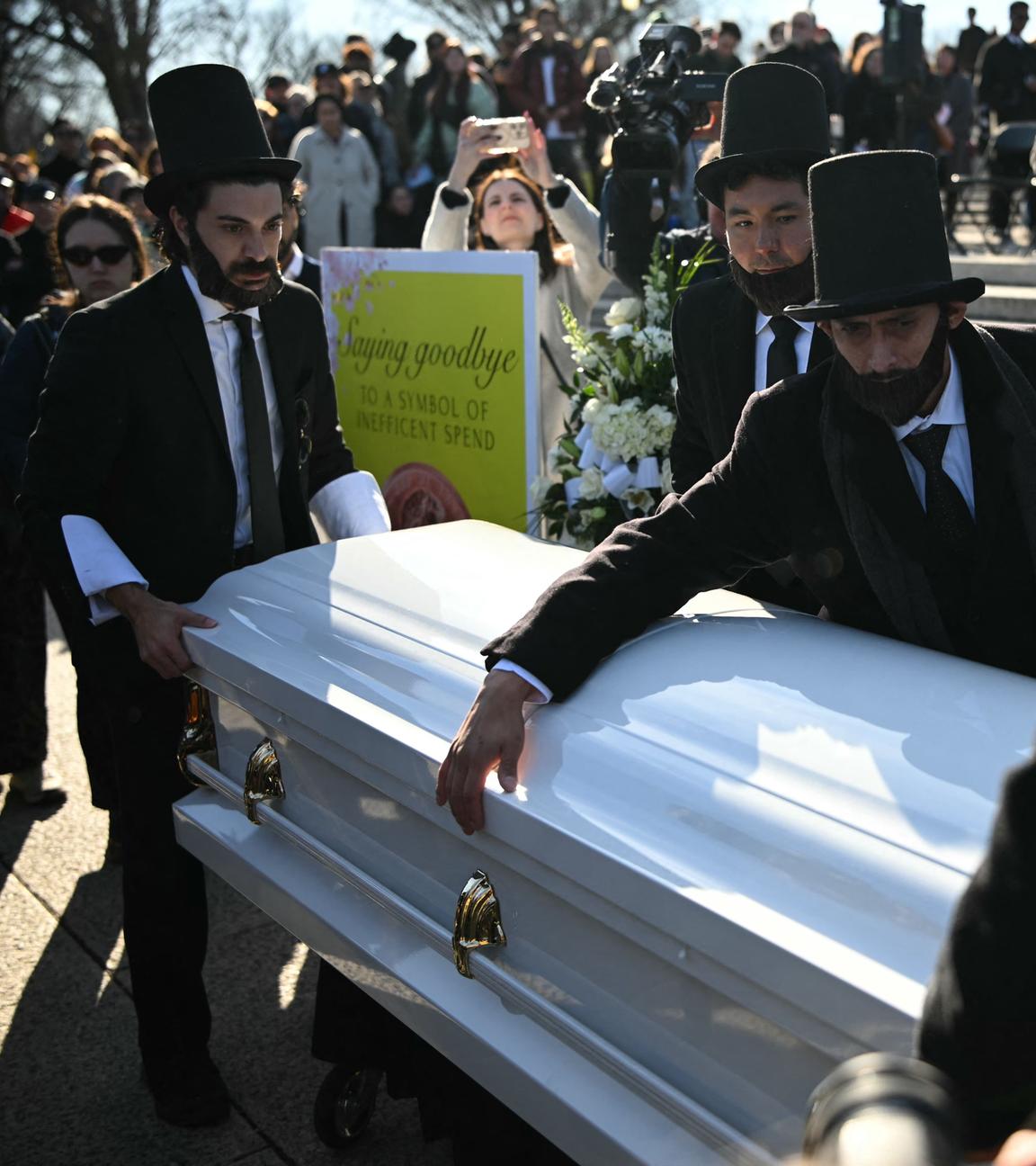 Männer, gekleidet wie der ehemalige US-Präsident Abraham Lincoln, öffnen einen Sarg, in den die Menschen während einer „Beerdigung“ für den Penny am Lincoln Memorial am 20. Dezember 2025 Pennys werfen können, um ihre Ehrerbietung zu erweisen.