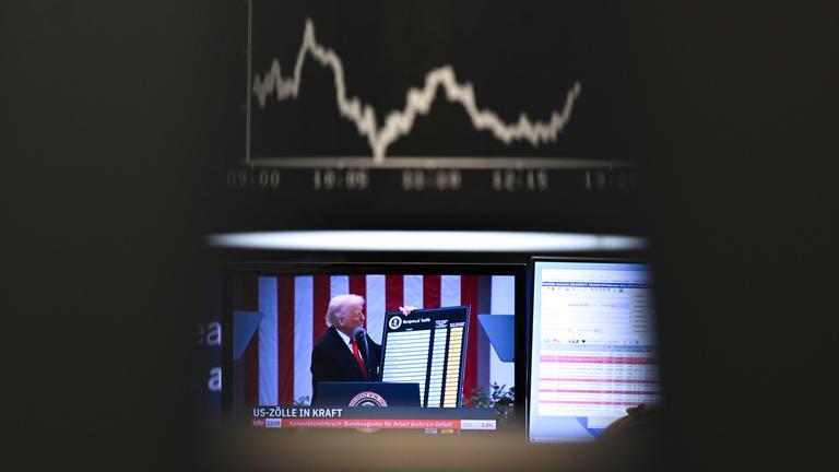 09.04.2025, Hessen, Frankfurt/Main: US-Präsident Trump ist auf einem Bildschirm auf dem Parkett der Frankfurter Wertpapierbörse vor der Anzeigetafel mit der Dax-Kurve zu sehen.