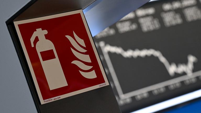 Hessen, Frankfurt/Main: Ein Hinweisschild für einen Feuerlöscher ist an einem Durchgang der Frankfurter Wertpapierbörse angebracht, während die Anzeigetafel mit der Dax-Kurve fallende Kurse anzeigt.