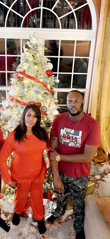 Es ist ein Familienfoto. Kuyateh und ihr erwachsener Sohn stehen vor einem beschmückten Weihnachtsbaum.