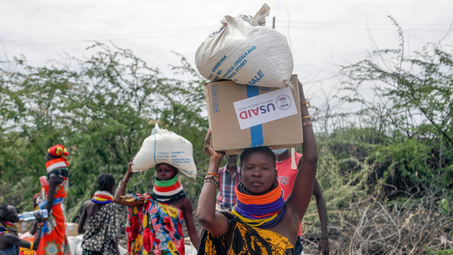 Frauen tragen Säcke mit Essen von USAID in Kenia.