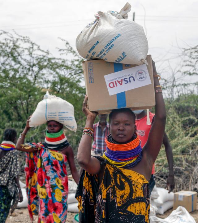 Frauen tragen Säcke mit Essen von USAID in Kenia.