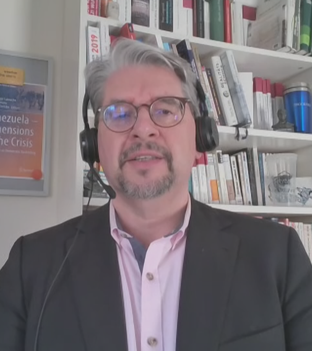 Lateinamerika-Experte Wolfgang Muno per Video zugeschaltet aus seinem Büro. Er trägt ein schwarzes Headset und im Hintergrund stehen voll Bücherregale.