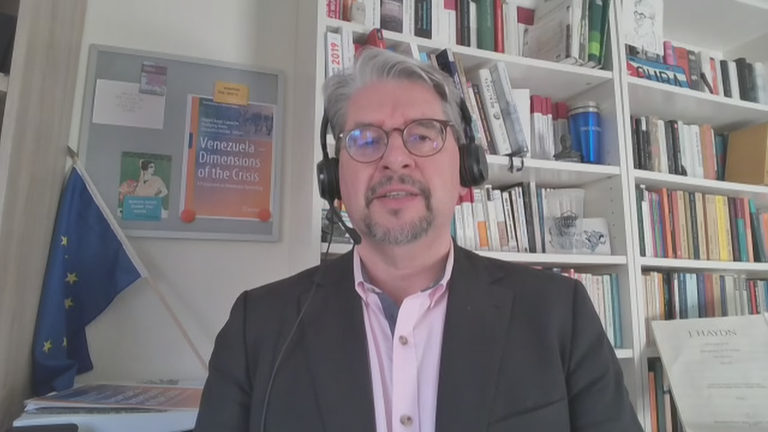 Lateinamerika-Experte Wolfgang Muno per Video zugeschaltet aus seinem Büro. Er trägt ein schwarzes Headset und im Hintergrund stehen voll Bücherregale.