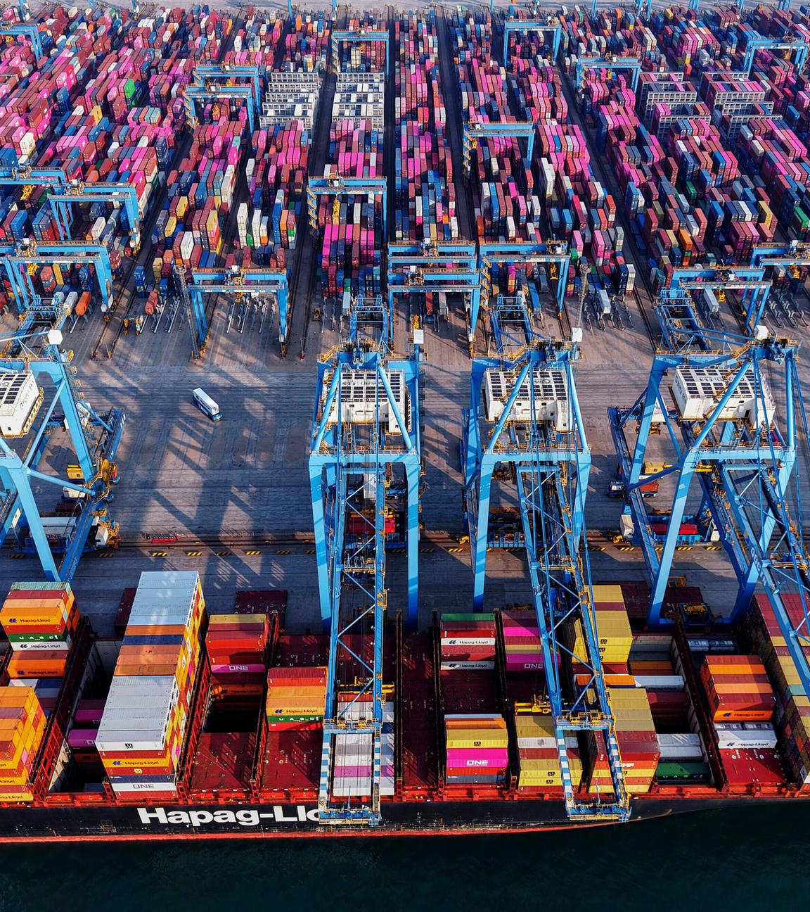 Lastwagen fahren in Qingdao in der ostchinesischen Provinz Shandong neben einem Schiff her, das Container in einem Containerterminal lädt.