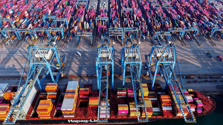 Lastwagen fahren in Qingdao in der ostchinesischen Provinz Shandong neben einem Schiff her, das Container in einem Containerterminal lädt.