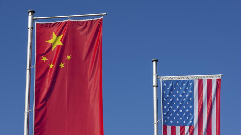 Chinesische und Amerikanische Flagge wehen vor einem klaren, blauen Himmel