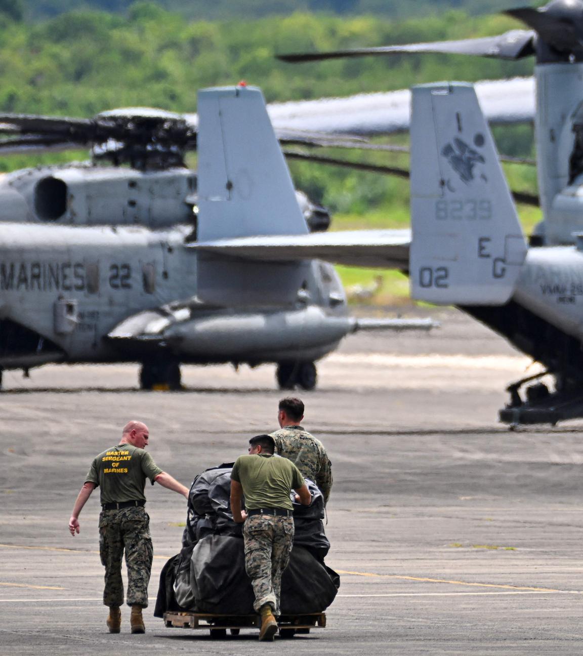 Militräflugzeuge und -hubschrauber und drei Soldaten, die etwas über das Rollfeld schieben.