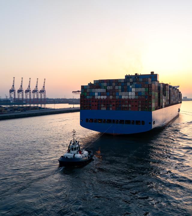 Luftaufnahme einer Drohne, die ein großes Containerschiff zeigt, das Hamburg auf der Elbe verlässt
