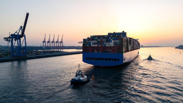 Luftaufnahme einer Drohne, die ein großes Containerschiff zeigt, das Hamburg auf der Elbe verlässt