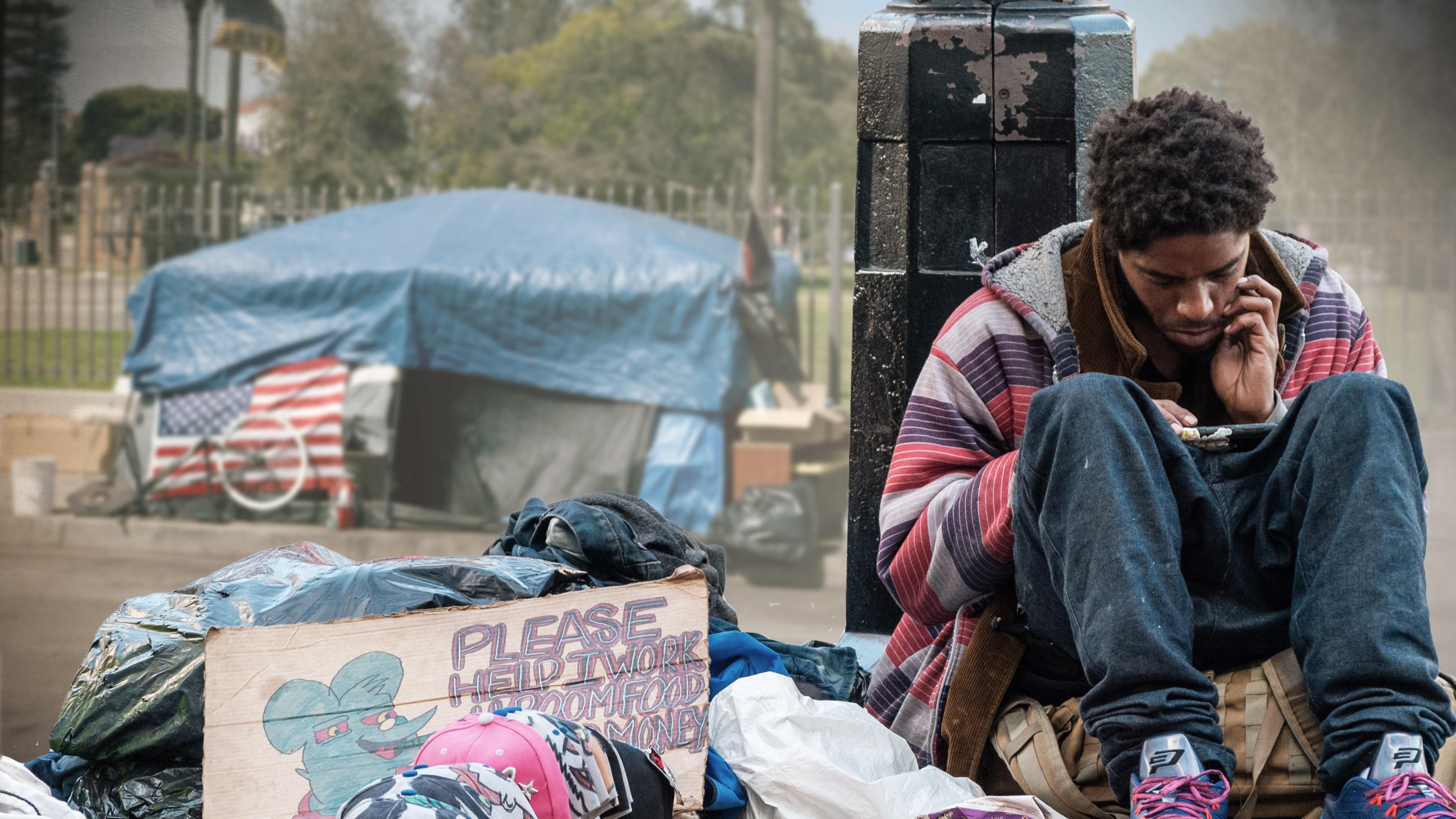 USA extrem: Obdachlos in Los Angeles": in der linken Bildhälfte improvisiertes Zelt aus Planen mit US-Fahne vor einem Zaun vor parkähnlichem Grundstück im Hintergrund, davor im Vordergrund Müllsäcke und Pappschild mit Schriftzug PLEASE HELP I WORK FOR ROOM FOOD MONEY und in der rechten Bildhälfte ein junger Mann, der auf einer Tasche sitzt, am unteren Teil einer Straßenlaterne lehnt und auf sein Smartphone schaut.