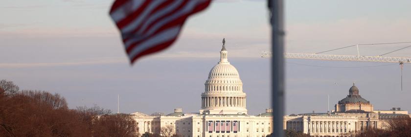 Die US-amerikanische Flagge weht im Vordergrund, weiter hinten ist das Kapitol in Washington zu sehen.
