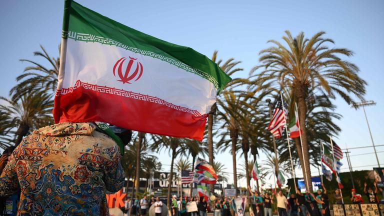 A man holds an Iranian flag in front of people holding pre-revolutionary Iranian flags outside Carson Sports Park before Irans training session in Los Angeles on June 14, 2026, on the eve of the 2026 World Cup football match between Iran and New Zealand.