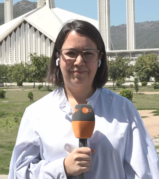 ZDF-Reporterin Phoebe Gaa vor einer Wiese mit Bäumen und einem weißen Gebäude in Islamabad