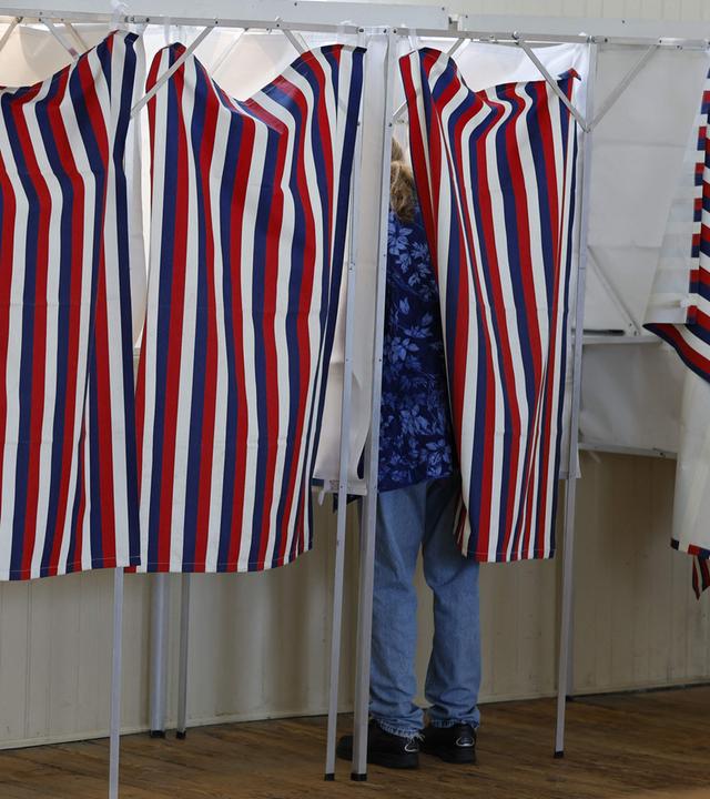 Von außerhalb der Wahlkabine sieht man eine Wählerin, die in der USA bei den Midterms in einer Wahlkabine steht.