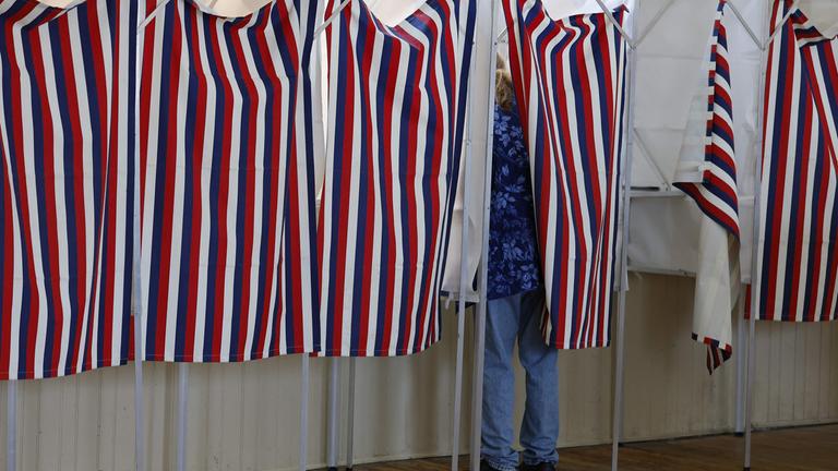 Von außerhalb der Wahlkabine sieht man eine Wählerin, die in der USA bei den Midterms in einer Wahlkabine steht.