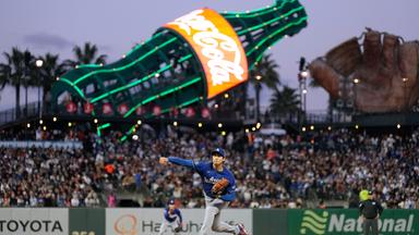 Shohei Ohtani, Pitcher der Los Angeles Dodgers, wirft einen Ball im Stadion. Im Hintergrund eine große Reklame von Coca-Cola.