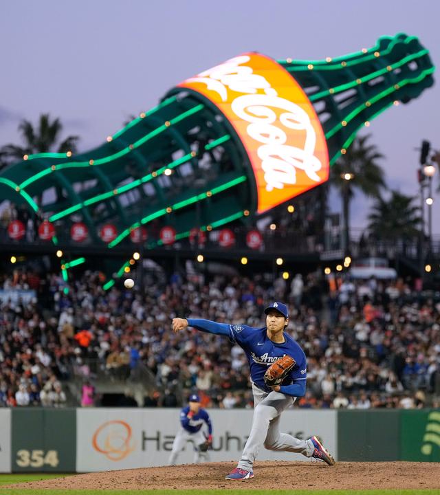 Shohei Ohtani, Pitcher der Los Angeles Dodgers, wirft einen Ball im Stadion. Im Hintergrund eine große Reklame von Coca-Cola.