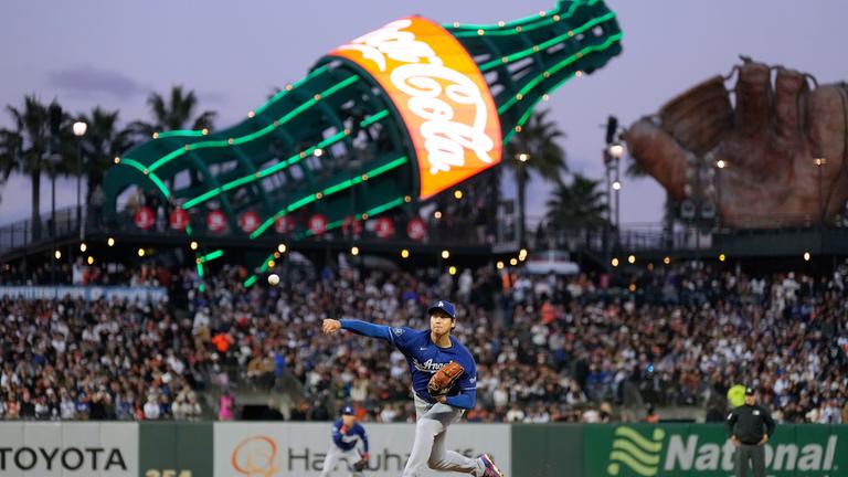 Shohei Ohtani, Pitcher der Los Angeles Dodgers, wirft einen Ball im Stadion. Im Hintergrund eine große Reklame von Coca-Cola.
