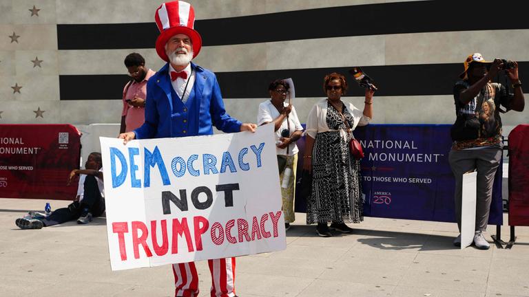 Ein Mann ist gekleidet in den Farben der USA und hält ein Demonstrationsplakat in den Händen.