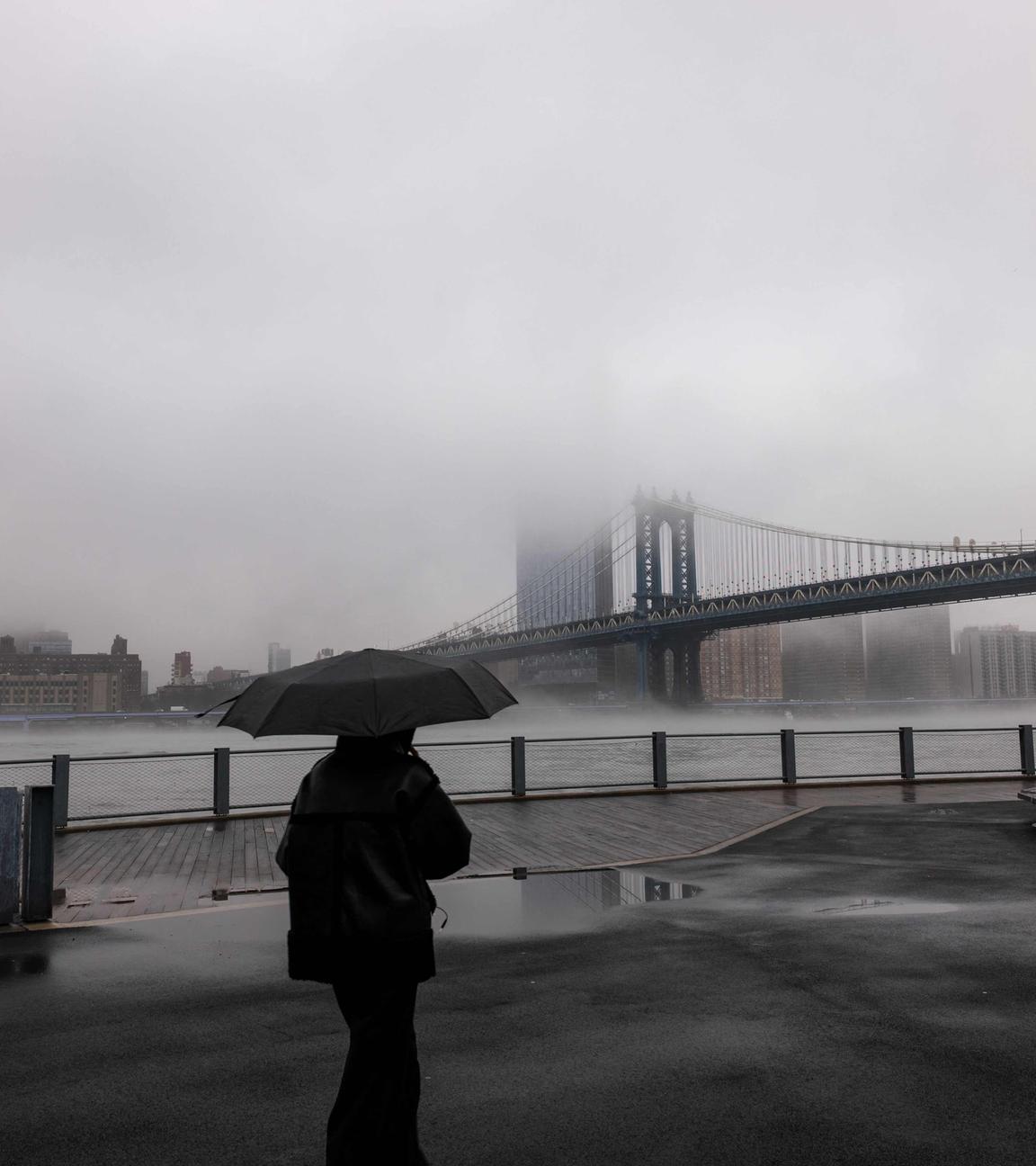Menschen gehen in New York City bei Regen und Nebel an der Manhattan Bridge vorbei.