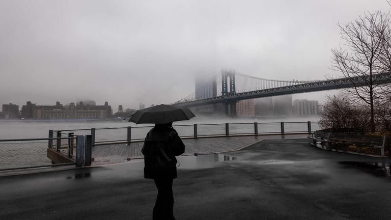 Menschen gehen in New York City bei Regen und Nebel an der Manhattan Bridge vorbei.