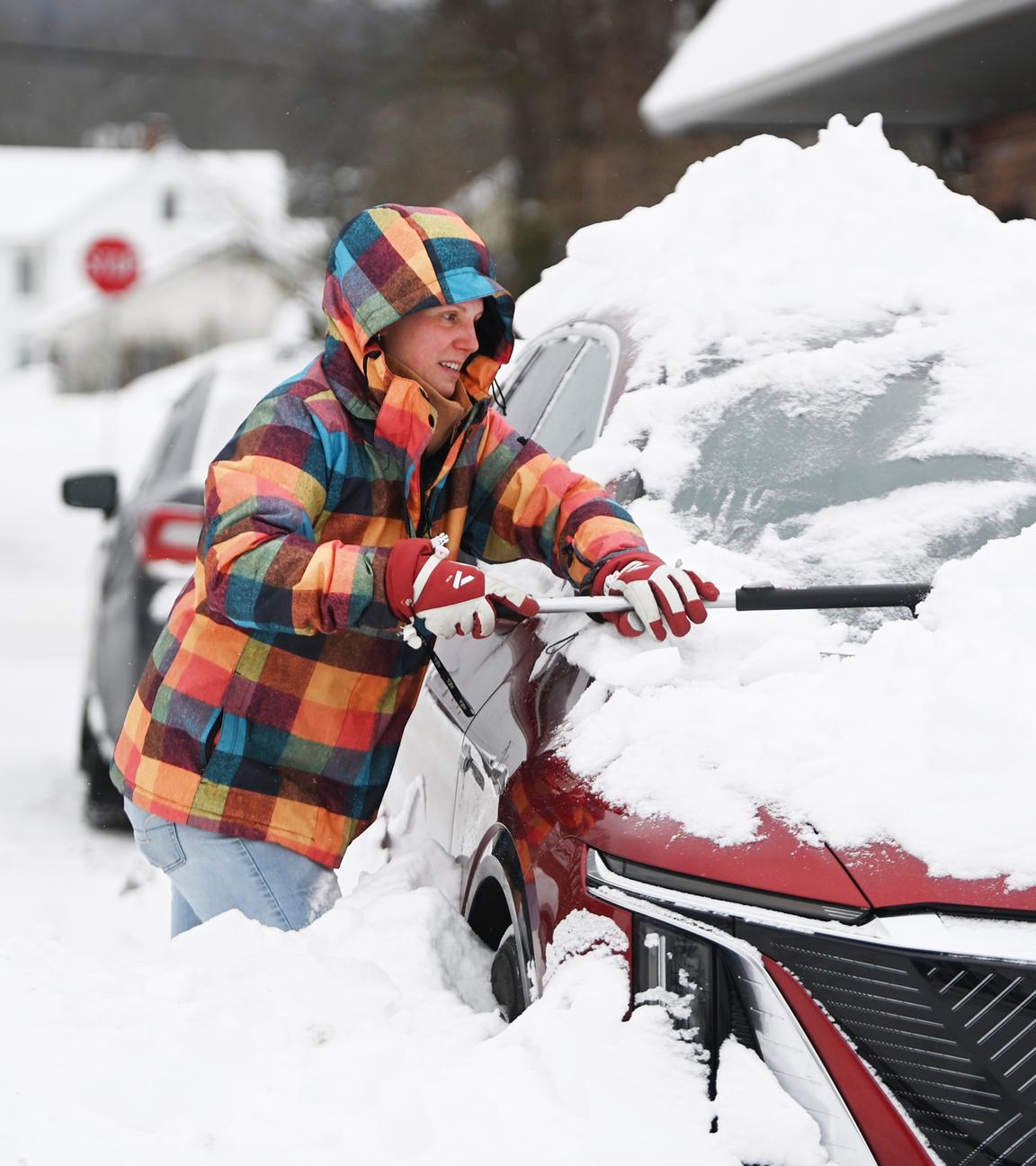Eine Frau versucht nach einem Wintersturm ein Auto vom Schnee zu befreien.