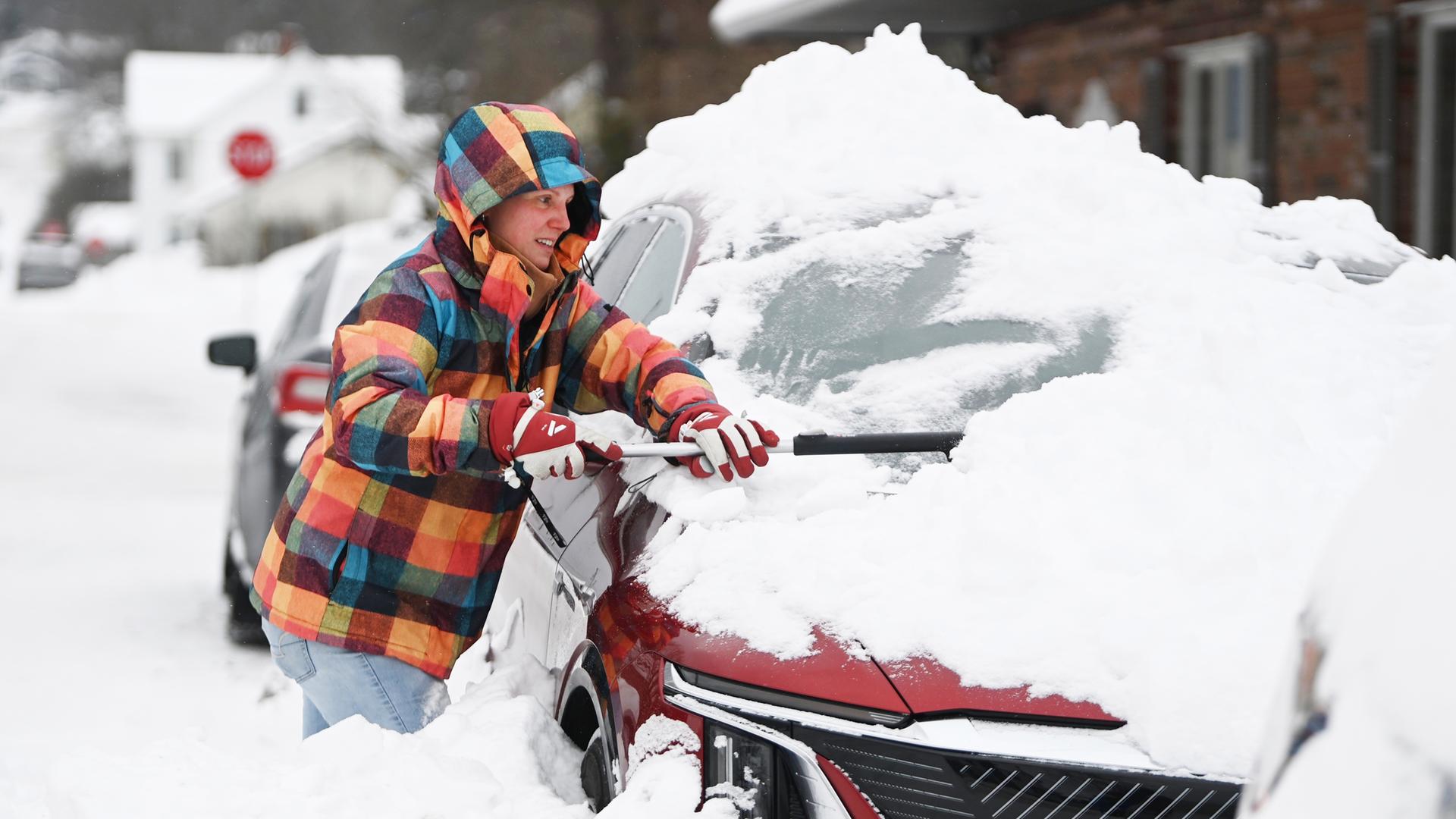 Eine Frau versucht nach einem Wintersturm ein Auto vom Schnee zu befreien.