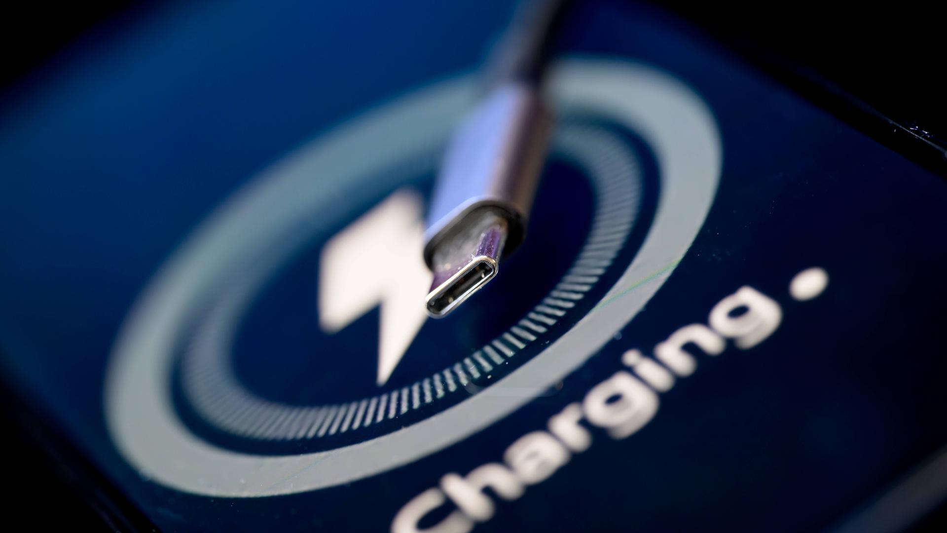 Ein USB-C Ladekabel liegt auf einem Bildschirm, auf dem das Wort "Charging" und eine Ladeanzeige mit Blitz leuchten.