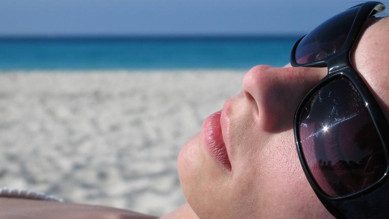 Eine Frau liegt mit einer Sonnenbrille am Strand.