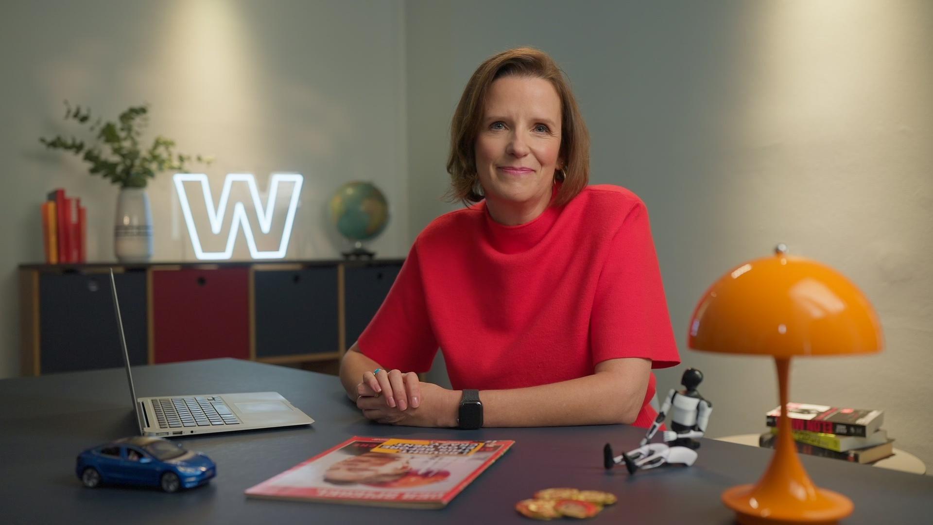 Valerie Haller sitzt in einem rotem Oberteil hinter einem Schreibtisch im Studio von "WISO - Wirtschaft erklärt".