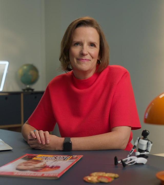 Valerie Haller sitzt in einem rotem Oberteil hinter einem Schreibtisch im Studio von "WISO - Wirtschaft erklärt".