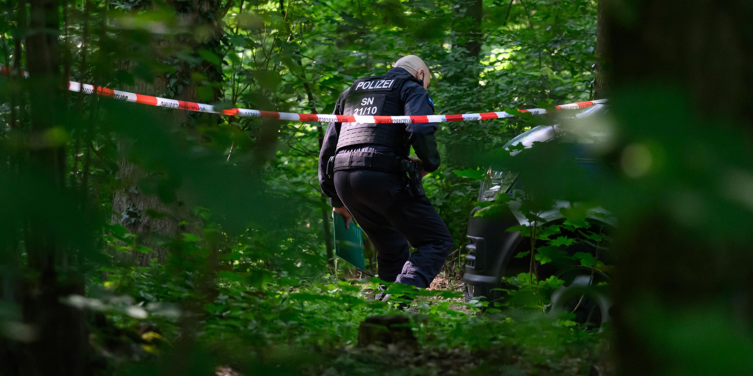 Ein Polizist geht in einem Wald unter Absperrband hindurch. 