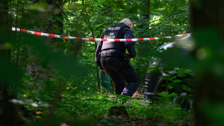 Ein Polizist geht in einem Wald unter Absperrband hindurch. 
