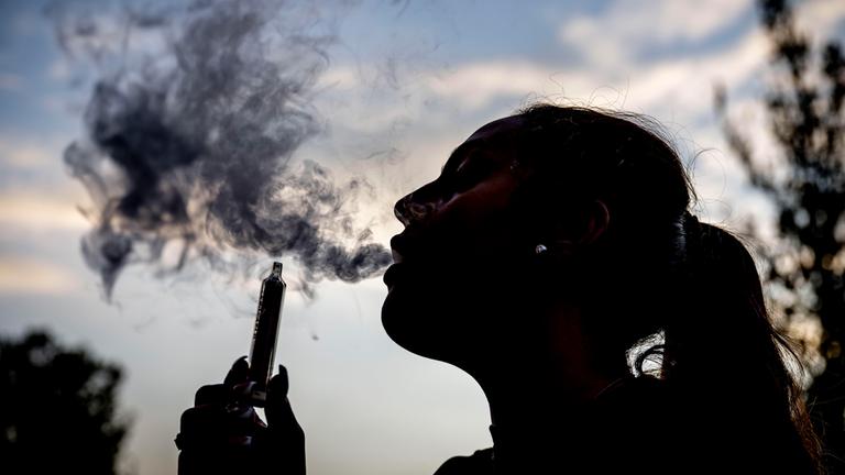 Eine junge Frau stößt den Rauch einer E-Zigarette aus.