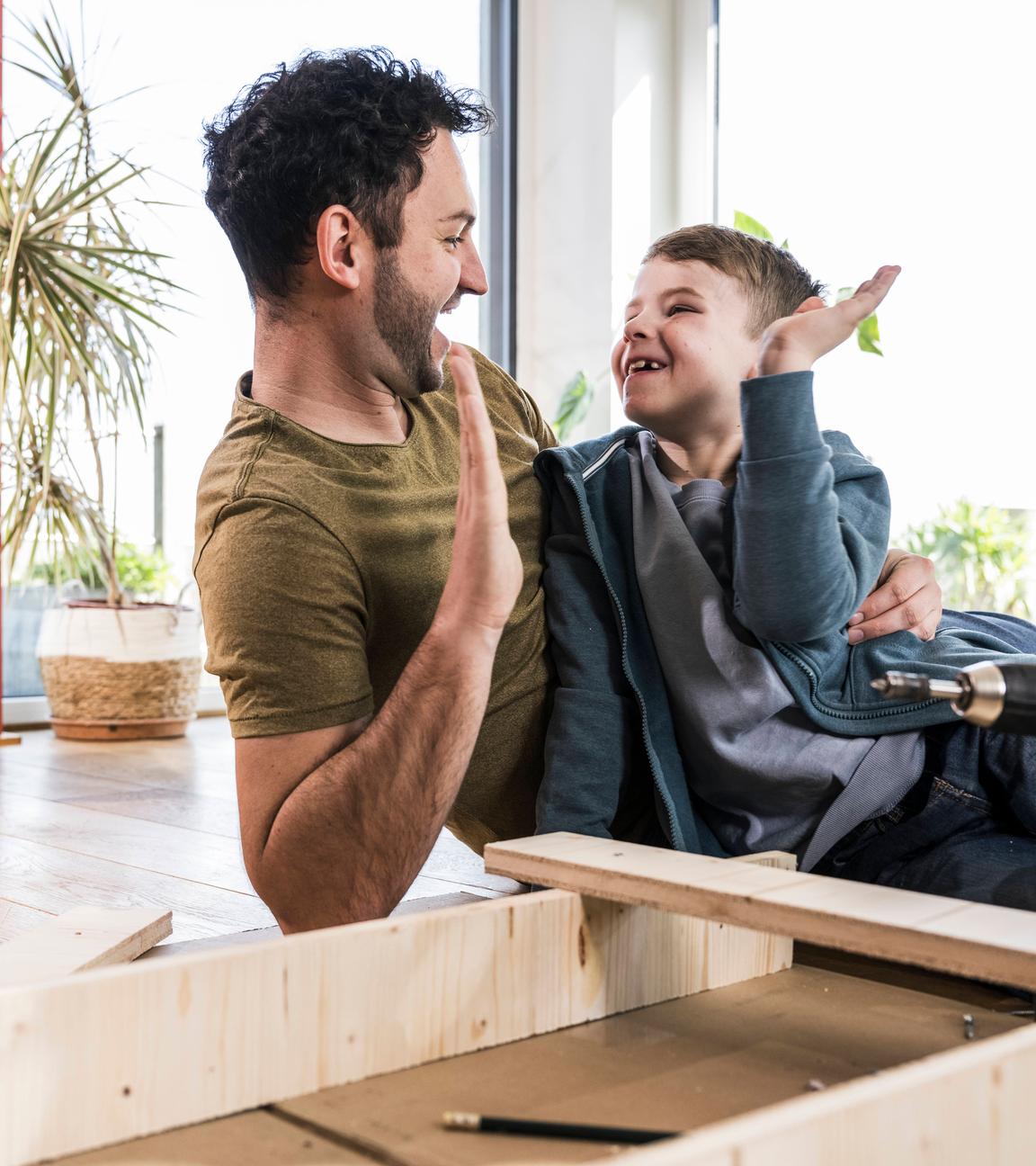 Vater und Sohn klatschen sich beim gemeinsamen Heimwerken in die Hände.