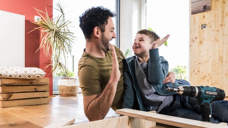 Vater und Sohn klatschen sich beim gemeinsamen Heimwerken in die Hände.