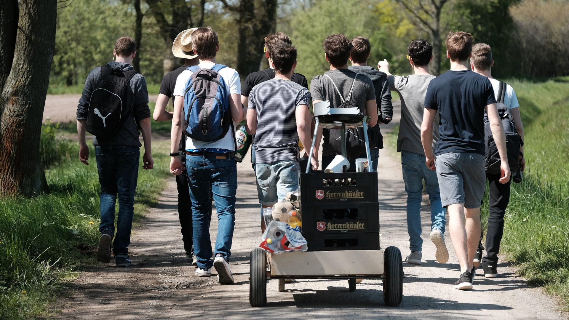Eine Gruppe junger Männer von hinten auf einer Vatertags-Wanderung mit Bollerwagen.
