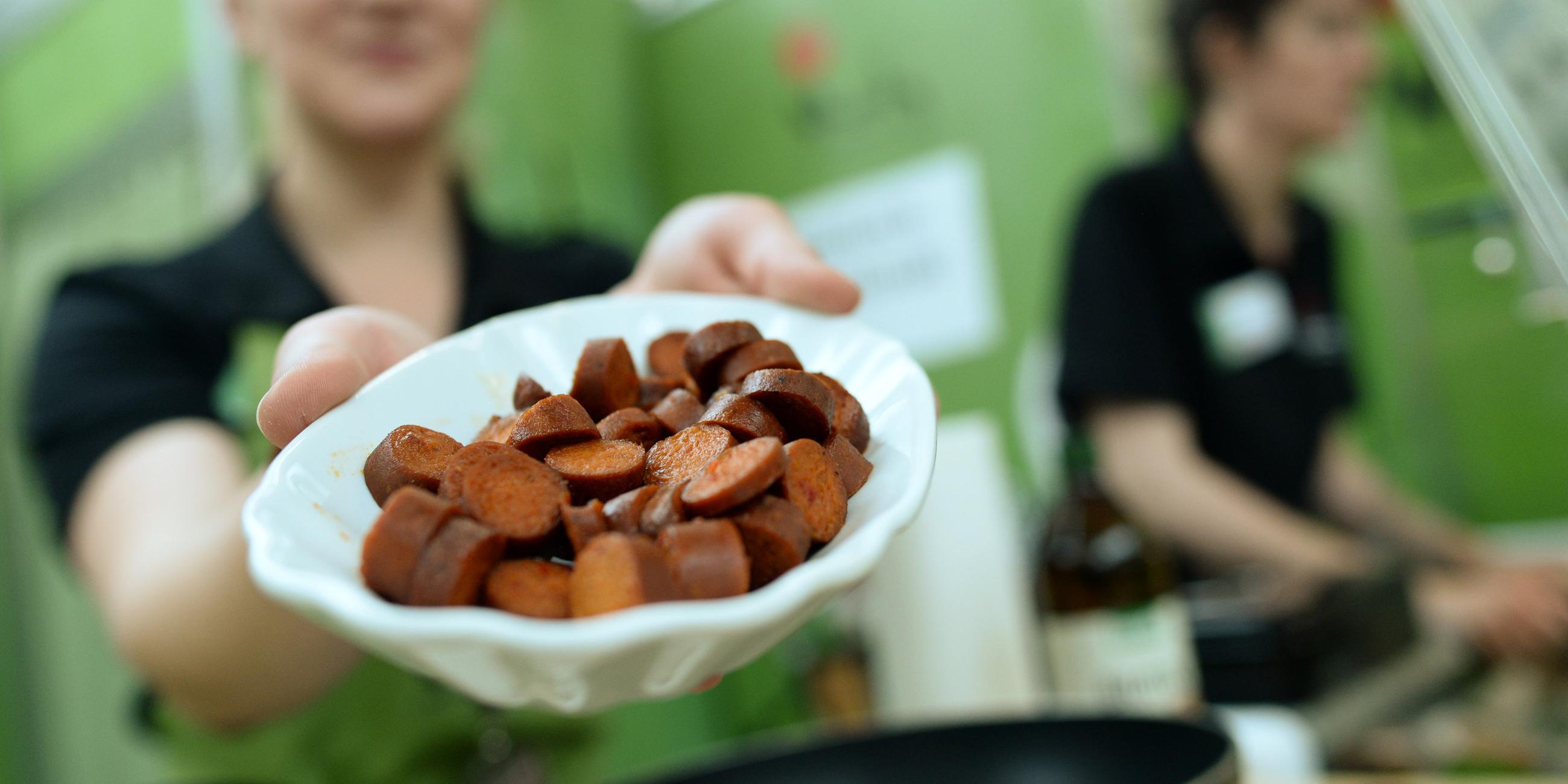 Eine Frau hält eine Schüssel mit einer aufgeschnittenen veganen Wurst in die Kamera.
