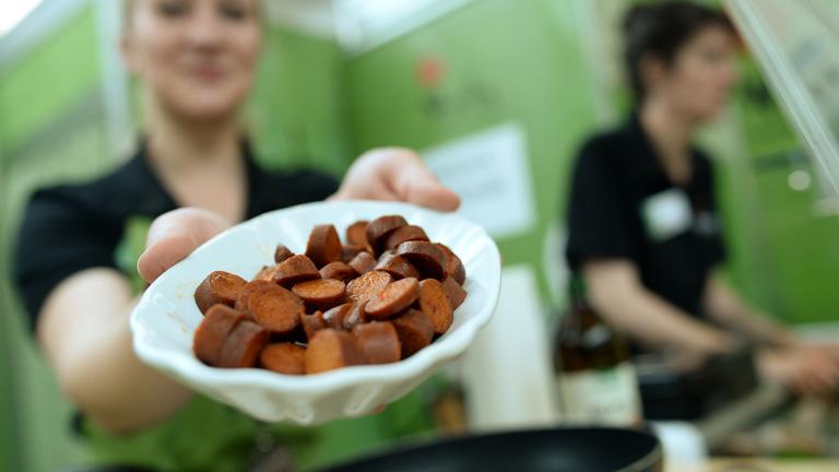 Eine Frau hält eine Schüssel mit einer aufgeschnittenen veganen Wurst in die Kamera.