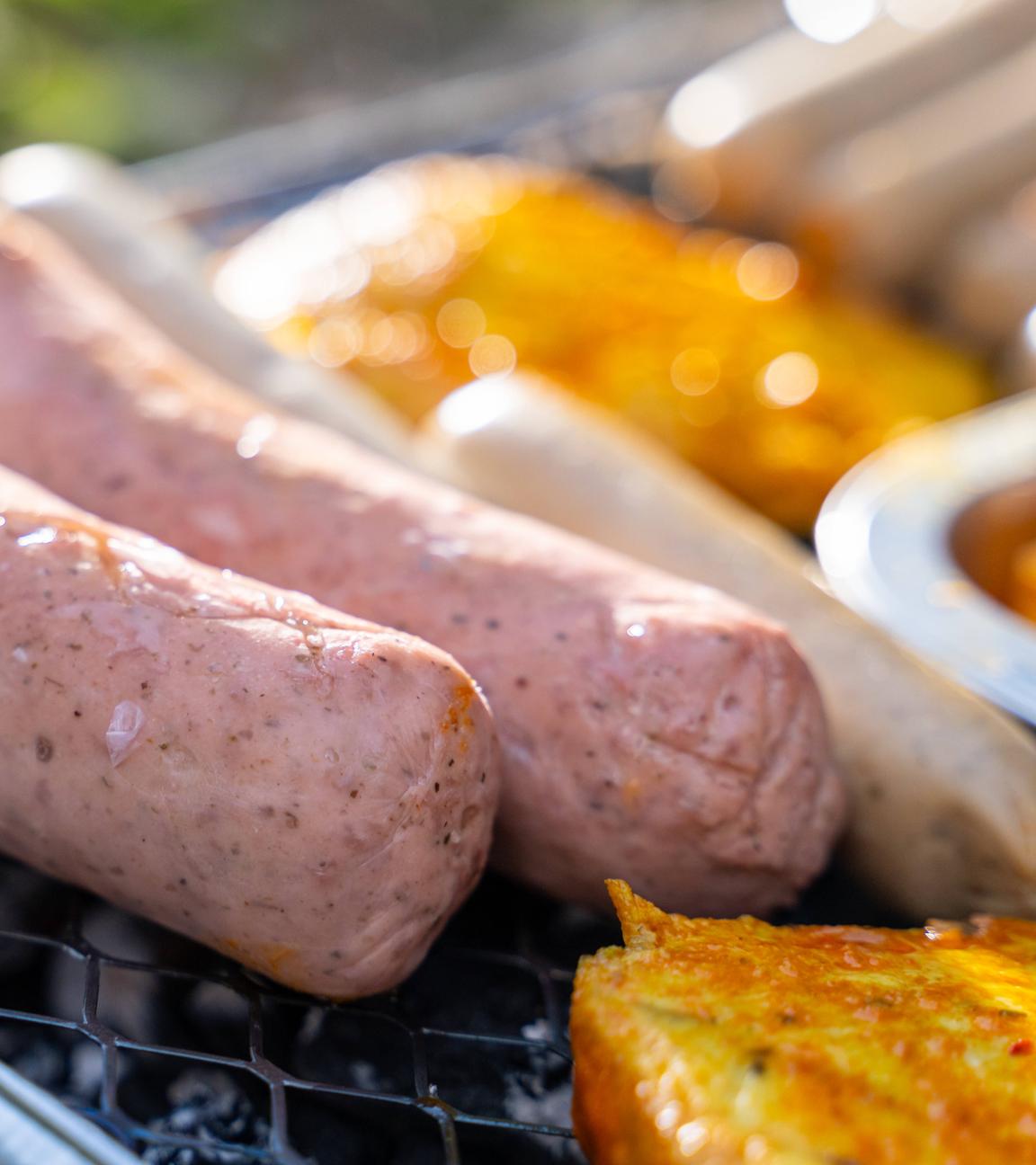 Rohe vegane Würstchen liegen neben Tofu-Stücken auf einem Grill.